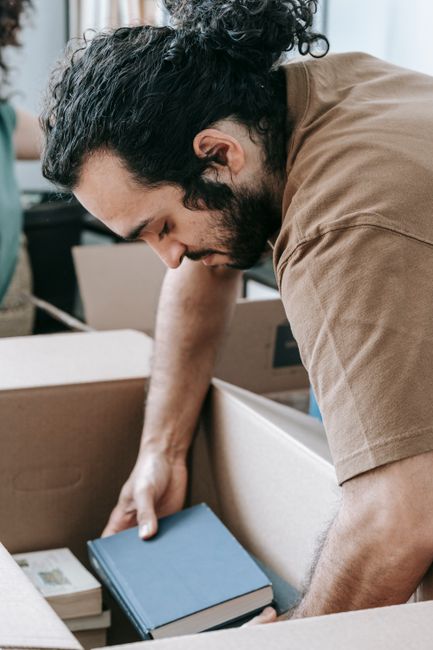 Two uniformed movers from Man With a Van Peckham are engaged in a furniture loading process, carefully carrying a large, dark green upholstered piece of furniture, possibly a sofa or armchair, into th